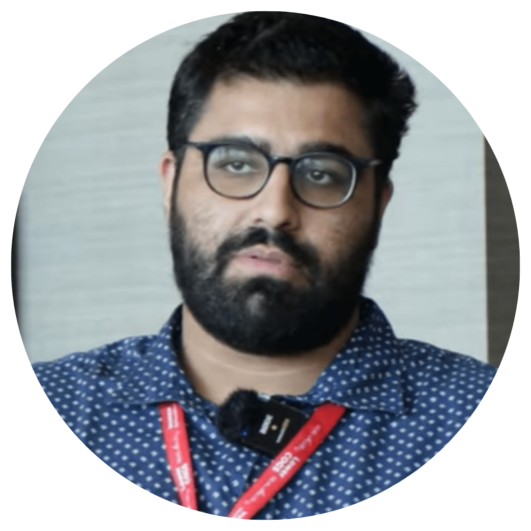 Portrait of a man with glasses and a beard wearing a blue polka-dot shirt and red lanyard in a circular crop.